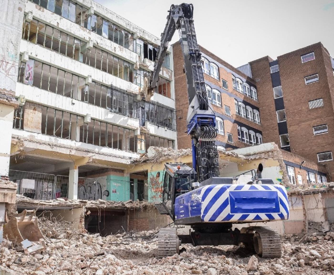 A high-reach demolition machine working on a multi-storey concrete frame, its
façade and floor slabs partly removed, with the arisings graded below.